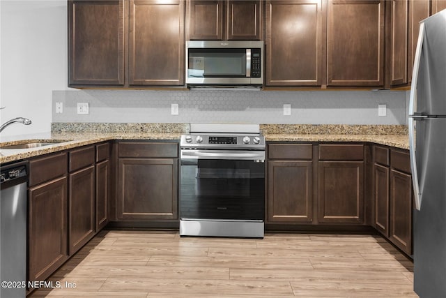 kitchen featuring sink, light hardwood / wood-style floors, light stone counters, dark brown cabinetry, and stainless steel appliances