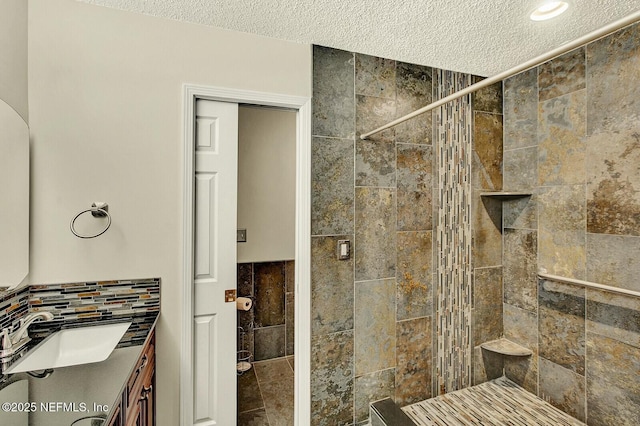 bathroom with a textured ceiling, vanity, tiled shower, and tile walls