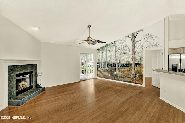 unfurnished living room featuring hardwood / wood-style flooring, vaulted ceiling, ceiling fan, and a tiled fireplace