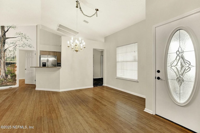 foyer featuring dark hardwood / wood-style flooring, an inviting chandelier, and vaulted ceiling