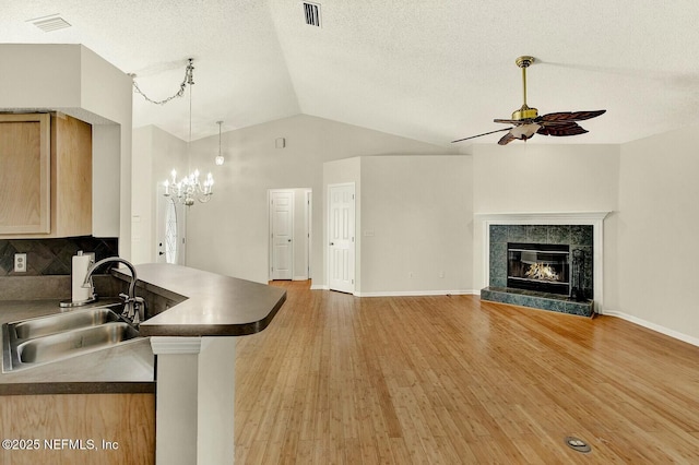 kitchen with ceiling fan with notable chandelier, sink, a tile fireplace, light brown cabinets, and lofted ceiling