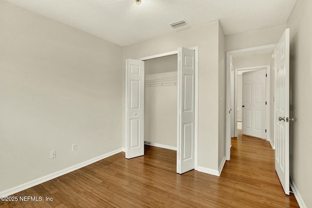 unfurnished bedroom with wood-type flooring, a textured ceiling, and a closet