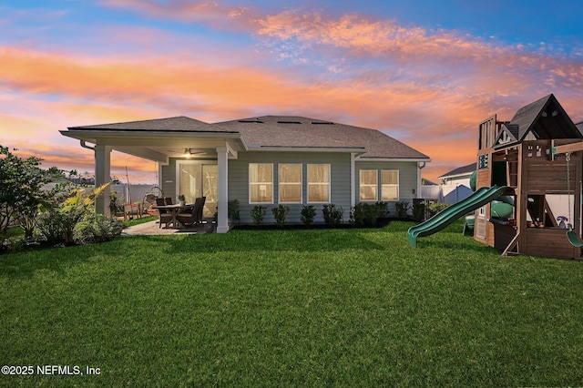 back house at dusk with a playground and a lawn