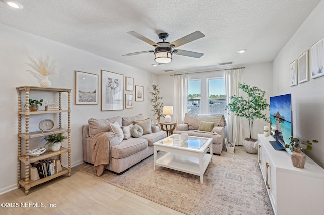 living room featuring ceiling fan, light hardwood / wood-style flooring, and a textured ceiling