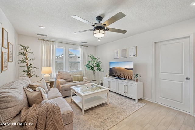 living room featuring ceiling fan, light hardwood / wood-style floors, and a textured ceiling