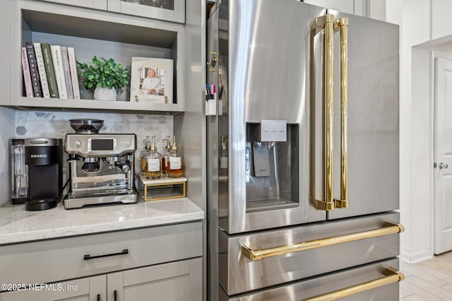 kitchen featuring backsplash, high quality fridge, light stone counters, and gray cabinetry