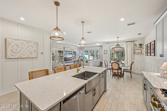 kitchen with decorative light fixtures, sink, an island with sink, and stainless steel appliances