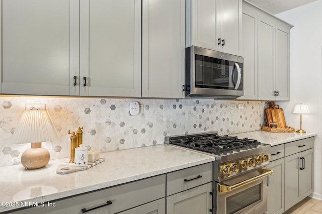 kitchen with backsplash, stainless steel appliances, light stone counters, and gray cabinets