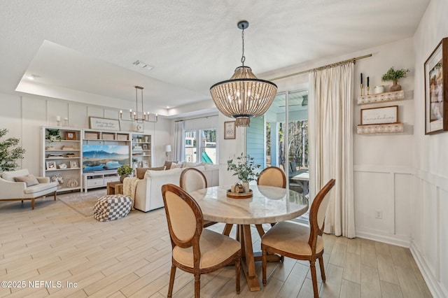 dining space with a raised ceiling, light wood-type flooring, a textured ceiling, and an inviting chandelier