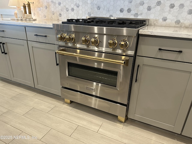 kitchen featuring gray cabinets, light stone countertops, high end stainless steel range oven, and tasteful backsplash