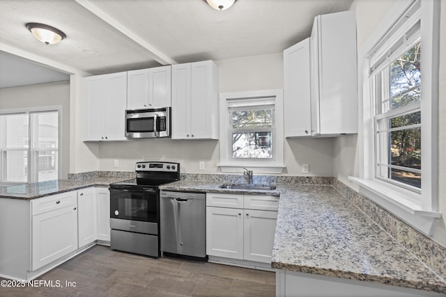 kitchen featuring light stone countertops, stainless steel appliances, white cabinetry, and sink