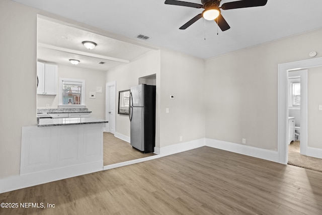 kitchen with stainless steel fridge, light wood-type flooring, ceiling fan, dark stone countertops, and white cabinets