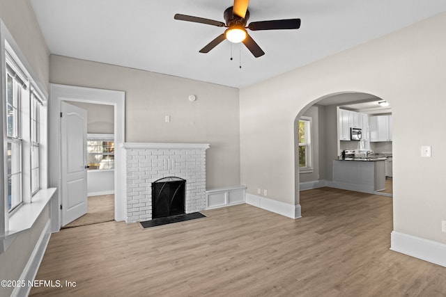 unfurnished living room with ceiling fan, light hardwood / wood-style floors, and a brick fireplace