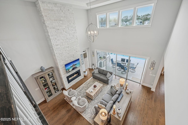 living room featuring dark hardwood / wood-style floors, a stone fireplace, a high ceiling, and an inviting chandelier