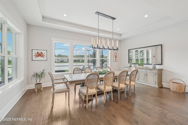 dining space with a raised ceiling, dark wood-type flooring, and an inviting chandelier