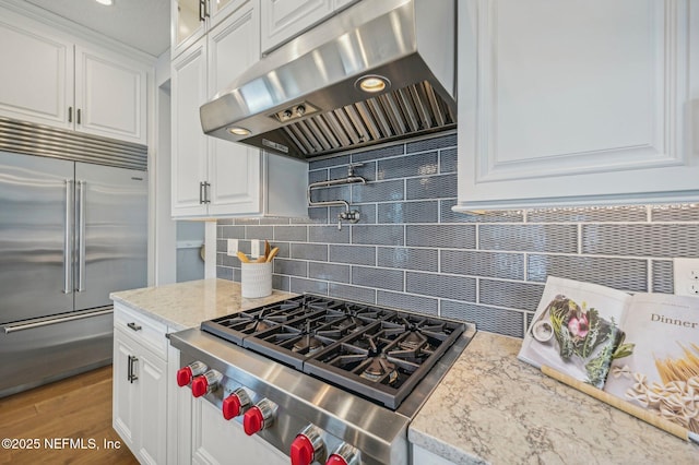 kitchen with white cabinetry, backsplash, built in refrigerator, stove, and exhaust hood