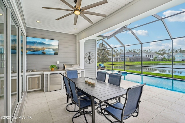 view of patio / terrace featuring glass enclosure, an outdoor kitchen, a water view, ceiling fan, and a grill