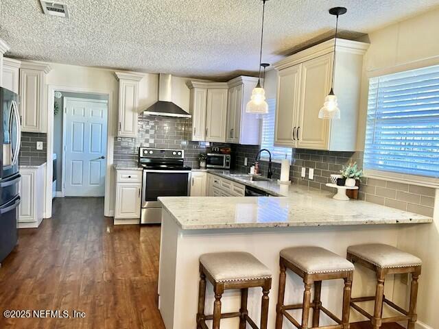 kitchen featuring pendant lighting, wall chimney exhaust hood, kitchen peninsula, and stainless steel appliances