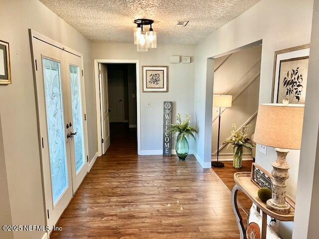 hallway with dark wood-type flooring, a textured ceiling, and french doors