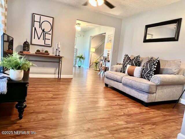 living room featuring hardwood / wood-style flooring, ceiling fan, and a textured ceiling