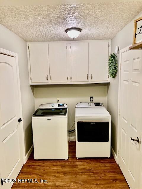 clothes washing area with dark wood-type flooring, cabinets, a textured ceiling, and independent washer and dryer