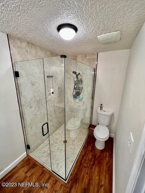 bathroom featuring hardwood / wood-style floors, a textured ceiling, toilet, and an enclosed shower