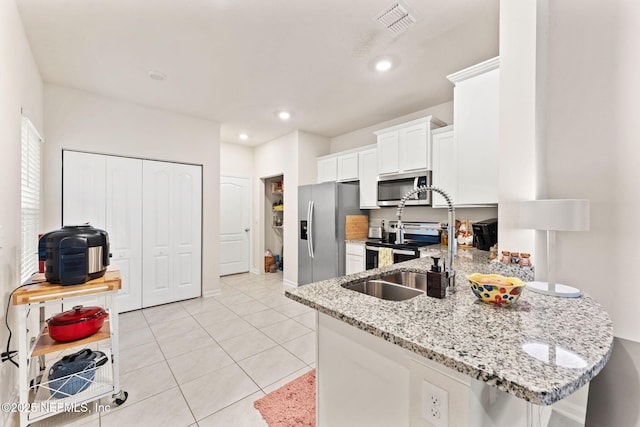 kitchen with light stone countertops, light tile patterned floors, kitchen peninsula, white cabinets, and appliances with stainless steel finishes