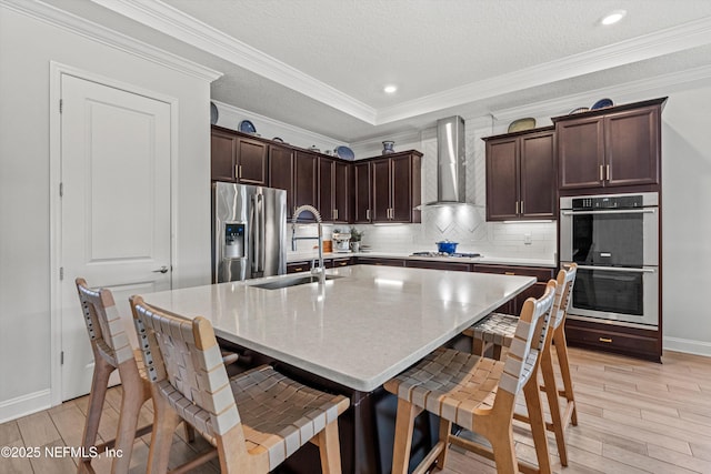 kitchen featuring a kitchen breakfast bar, wall chimney range hood, stainless steel appliances, and a center island with sink