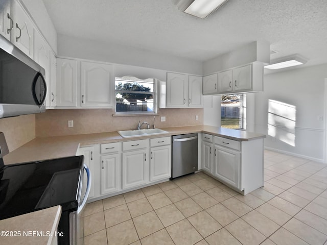 kitchen featuring kitchen peninsula, stainless steel appliances, sink, light tile patterned floors, and white cabinets