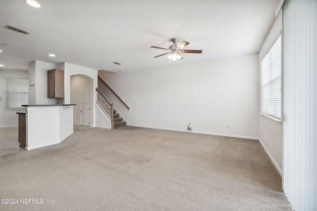 unfurnished living room featuring a textured ceiling, plenty of natural light, ceiling fan, and light carpet