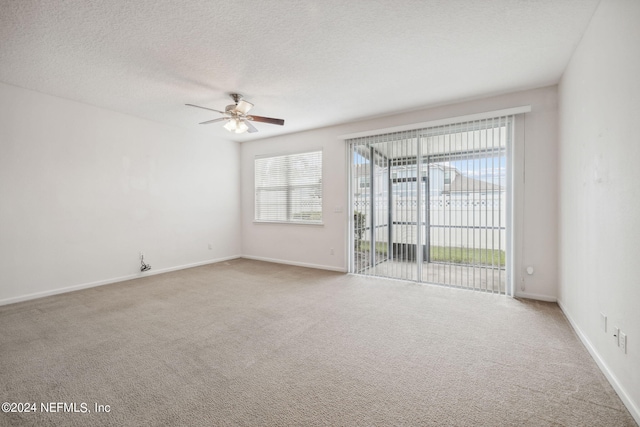 empty room with a wealth of natural light, ceiling fan, light colored carpet, and a textured ceiling