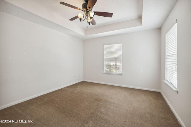 carpeted empty room featuring ceiling fan and a raised ceiling