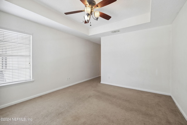 unfurnished room with carpet, a tray ceiling, plenty of natural light, and ceiling fan