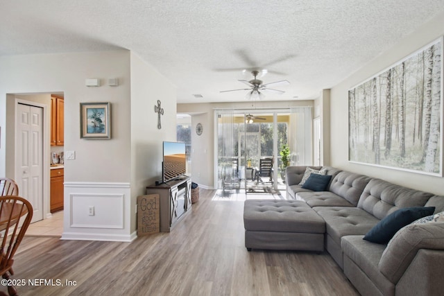 living room with a textured ceiling, light hardwood / wood-style floors, and ceiling fan