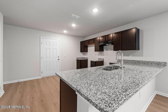 kitchen with kitchen peninsula, light stone countertops, dark brown cabinetry, sink, and light hardwood / wood-style flooring