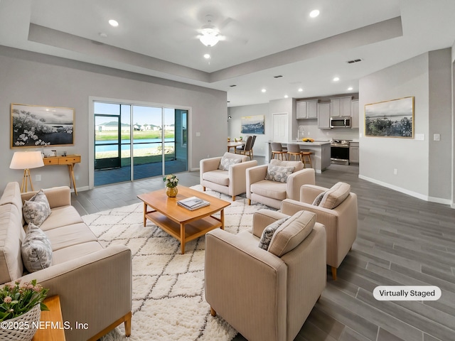 living room with a raised ceiling, ceiling fan, and wood-type flooring