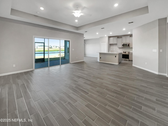 unfurnished living room featuring a tray ceiling and ceiling fan