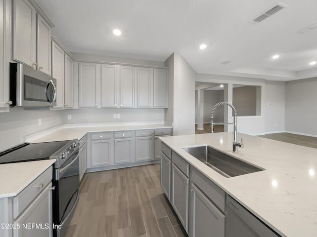 kitchen featuring light stone counters, stainless steel appliances, sink, hardwood / wood-style floors, and gray cabinets