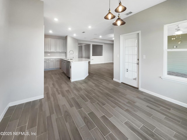 kitchen featuring ceiling fan, sink, hanging light fixtures, dark hardwood / wood-style flooring, and a center island with sink