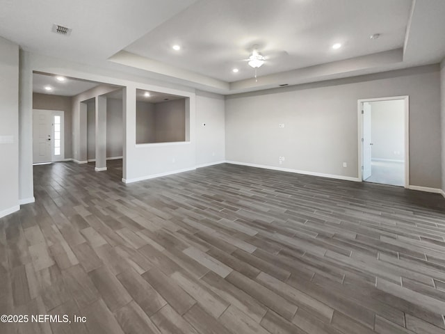 unfurnished living room with dark hardwood / wood-style floors, ceiling fan, and a raised ceiling