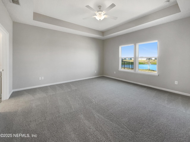 carpeted spare room with ceiling fan, a water view, and a tray ceiling