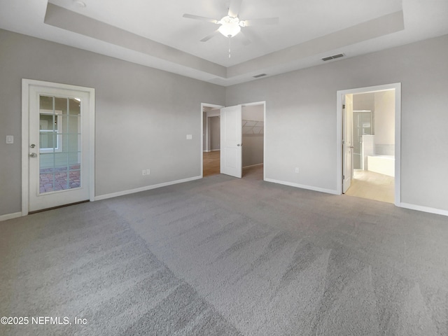 unfurnished bedroom featuring carpet flooring, ceiling fan, a spacious closet, a tray ceiling, and a closet