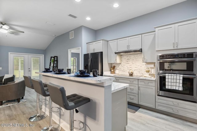 kitchen with french doors, stainless steel appliances, vaulted ceiling, ceiling fan, and a breakfast bar area