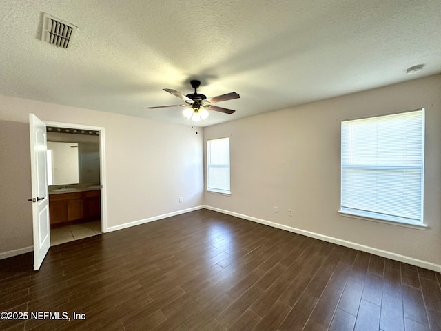 interior space with a textured ceiling, ensuite bath, ceiling fan, and dark wood-type flooring