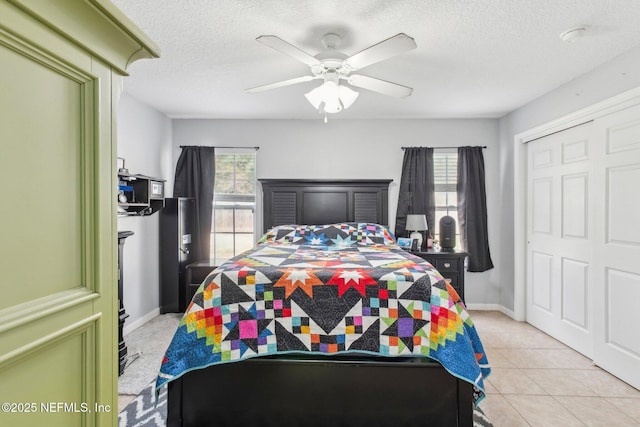 bedroom featuring ceiling fan, a closet, light tile patterned flooring, and a textured ceiling