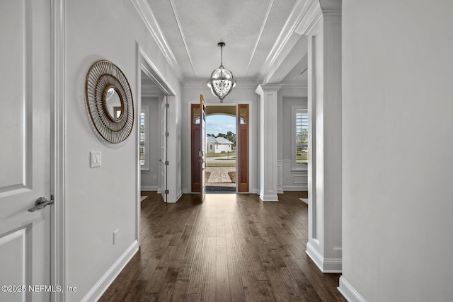 foyer with decorative columns, crown molding, dark wood-type flooring, and an inviting chandelier