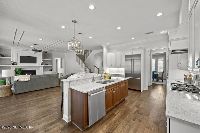 kitchen with light stone counters, stainless steel appliances, decorative light fixtures, white cabinets, and an island with sink