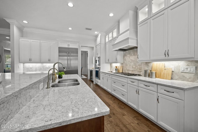 kitchen featuring white cabinets, sink, built in appliances, light stone counters, and custom range hood