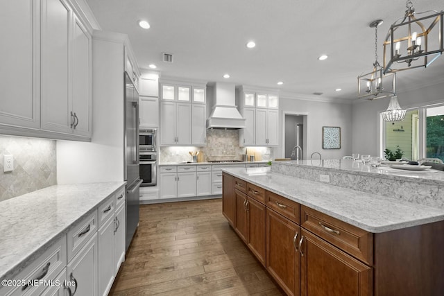 kitchen featuring appliances with stainless steel finishes, decorative light fixtures, white cabinetry, and custom exhaust hood