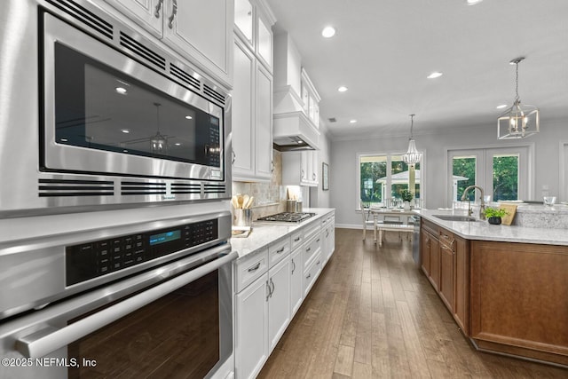 kitchen with white cabinetry, sink, light stone countertops, custom range hood, and appliances with stainless steel finishes